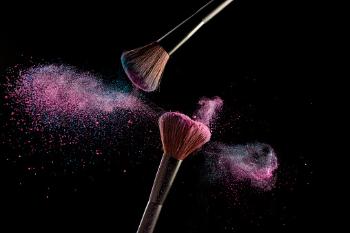 Make-up brushes with pink and blue powder explosion on black background