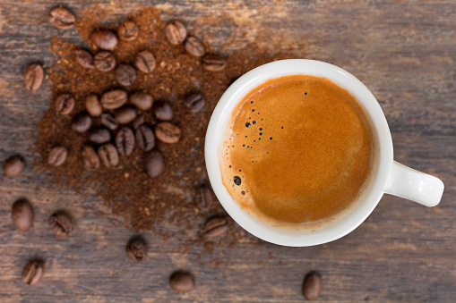 A cup of espresso top view, blur coffee beans with ground on wooden background.