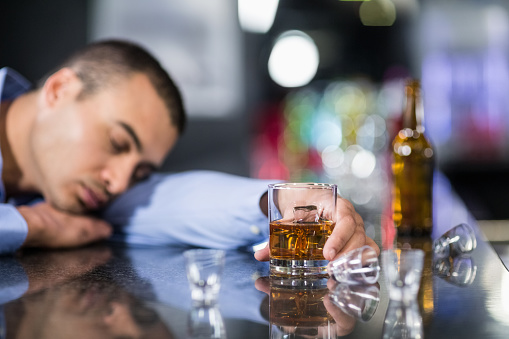 Tired man having a whiskey and sleeping on a counter in a pub