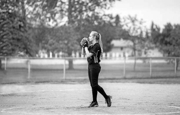 Teenage girl in fastball pitching stance A teenage girl in fast ball pitching stance on the pitchers mound in uniform in black and white softball pitcher stock pictures, royalty-free photos & images