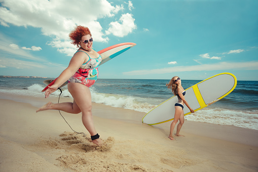 Beautiful young fat woman is runing to the summer sea with the surfboard