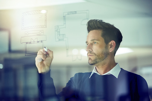 Shot of a businessman drawing on a glass wall in an office