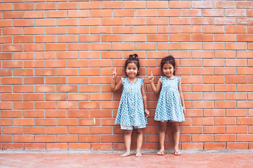 Portrait of two asian kid girls pointing up on brick wall background in vintage color tone