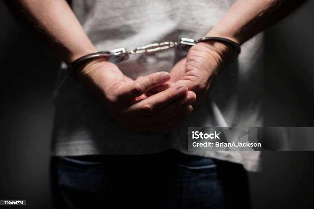 Criminal in handcuffs Arrested man in handcuffs with handcuffed hands behind back Police Force Stock Photo