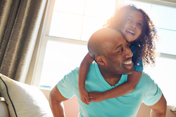 Never a dull moment when you're around Shot of a happy little girl hugging her father from behind while he sits on the couch at home child candid indoors lifestyles stock pictures, royalty-free photos & images