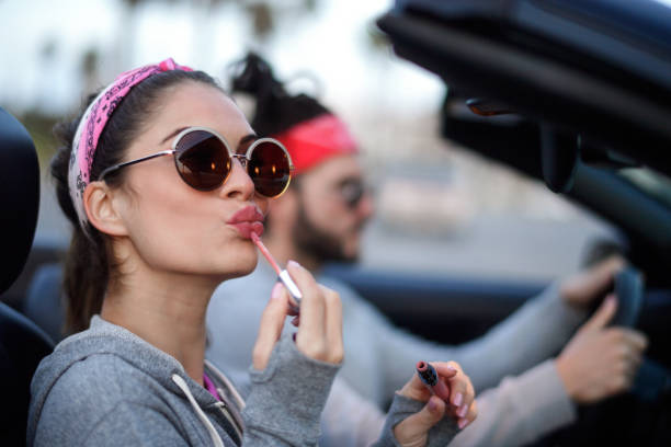 Young couple in the car Young heterosexual couple in the city driving in a car and having fun. Woman is applying lip gloss. hipster car stock pictures, royalty-free photos & images