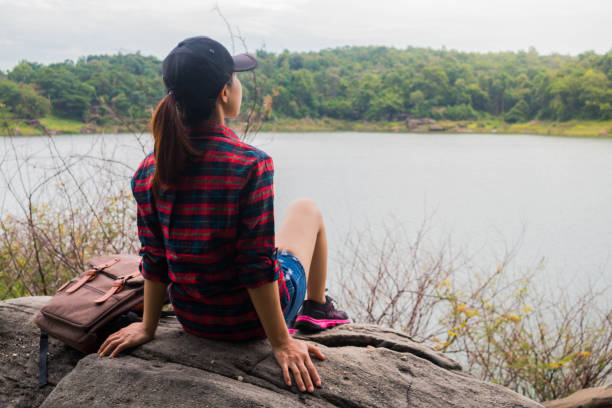 istock Woman with backpack sit by the the riverside. 700664374
