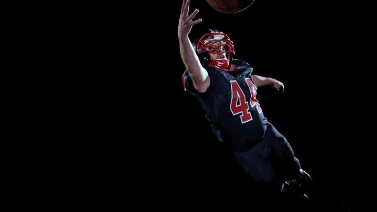 SLO MO American football player in black jersey catching the ball in the air with one hand on black background