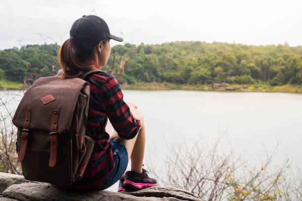 istock Woman with backpack sit by the the riverside. 700665594