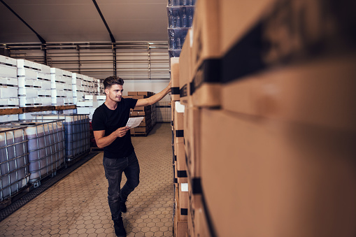 Young man taking the stock of packaged beer boxed in warehouse. Warehouse manager taking finished goods inventory at brewery.