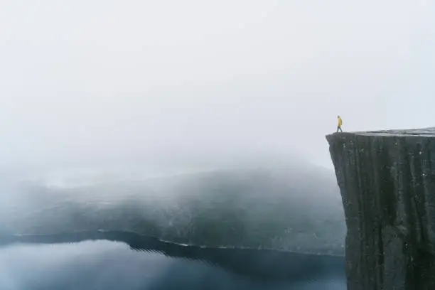 Photo of Man in yellow raincoat on the Preikestolen in fog in Norway
