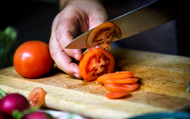 istock Closeup of hand with knife cutting fresh vegetable tomato 700685630