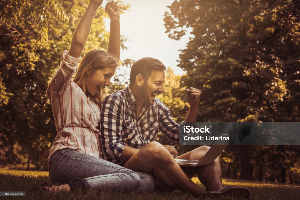 Young couple sitting  on the grass. Happy couple using laptop. Laptop Stock Photo