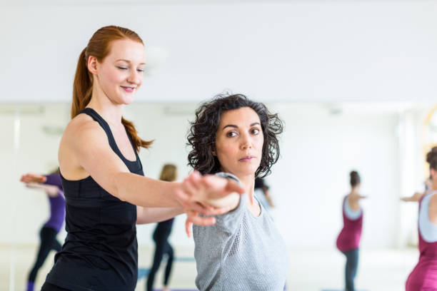 Professional yoga trainer supporting woman in health club Professional yoga trainer supporting woman during stretching workout. Young beautiful female instructor coaching student in fitness club. yoga instructor stock pictures, royalty-free photos & images
