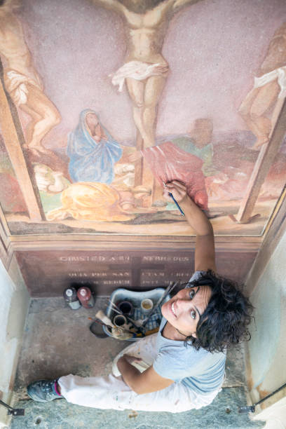 реставратор работает над античной наружной фреской часовни в италии: восстановление живописи религиозного искусства - restoring painting working church стоковые фото и изображения