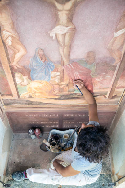 реставратор работает над античной наружной фреской часовни в италии: восстановление живопи�си религиозного искусства - restoring painting working church стоковые фото и изображения