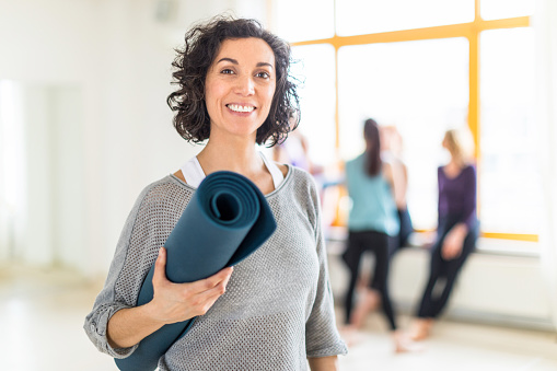 Happy mature woman holding a yoga mat in health club. Fitness female after work out session in gym.