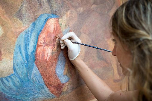 Restorer working on antique outdoor chapel fresco in Italy: Painting restoring of religious art