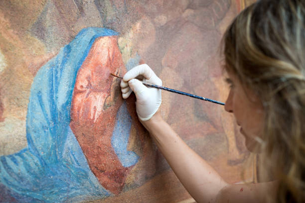Restorer working on antique outdoor chapel fresco in Italy: Painting restoring of religious art Restorer working on antique outdoor chapel fresco in Italy: Painting restoring of religious art protective glove photos stock pictures, royalty-free photos & images