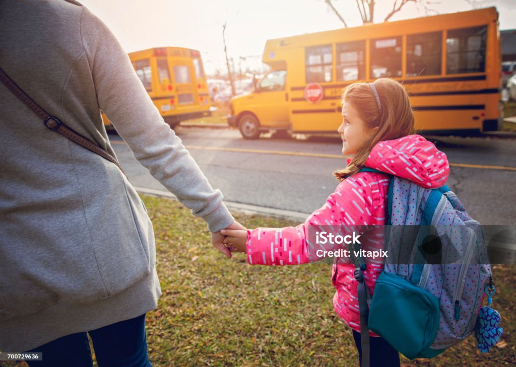 Mother Seeing Her Daughter Off to School Mother Seeing Her Daughter Off to School. Waiting for school bus to pick her up, holding hands. School Bus Stock Photo