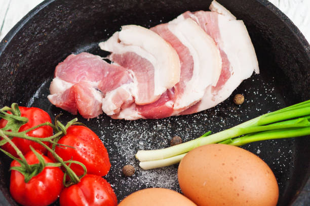 istock Cherry tomatoes on a branch, yellow eggs, bacon and spring onions lie on a rustic table next to a black frying pan 700749676