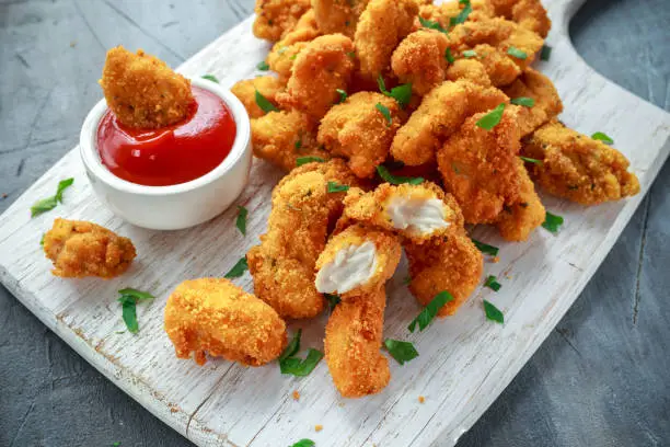 Fried crispy chicken nuggets with ketchup on white board.