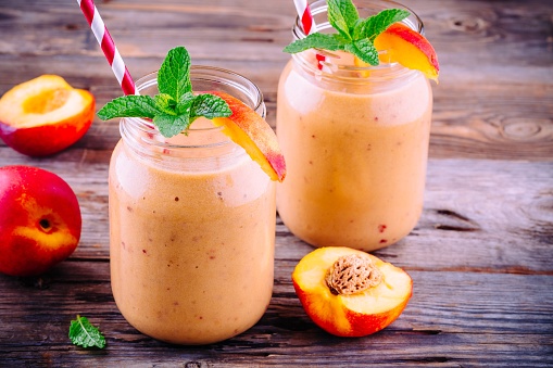 Healthy nectarine smoothies in a mason jar with mint on wooden rustic background