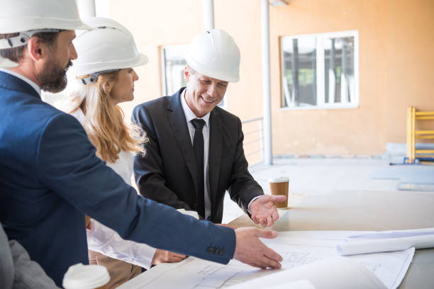 istock mature contractors in formal wear working with blueprints at construction 700777350