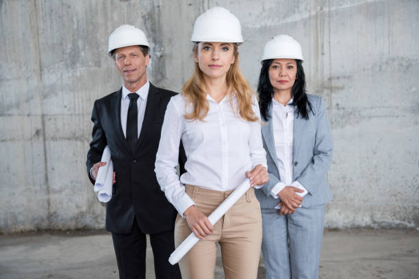 istock Professional team of architects in helmets holding blueprints and looking at camera 700799456