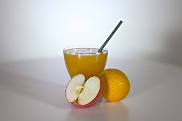 There is a glass with juice standing on a kitchen table. Half of the apple and a lemon are next to it.