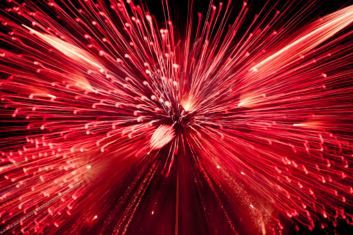Abstract, blurry, bokeh-style colorful photo of fireworks in a red tone above the river