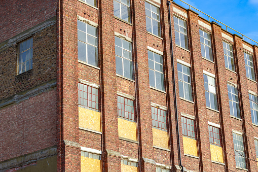 Windows on brick warehouse facade with ventilation fan. Building repurposed for other uses with original windows boarded up.