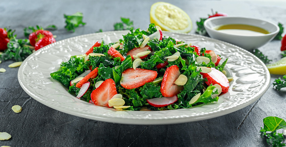 Healthy kale salad with strawberries and almond in a white plate.