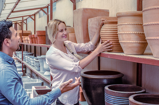 Male and positive young woman customers choosing crockery in ceramics workshop