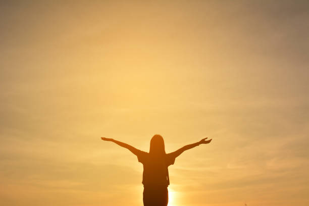 istock Silhouetted Woman With Arms Outstretched Against Sky During Sunset 700841867