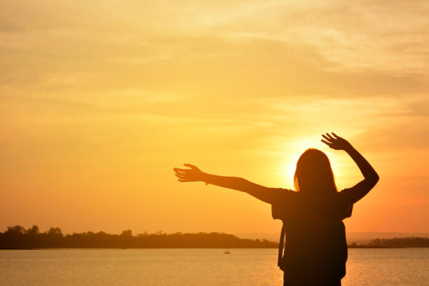 istock Silhouetted Woman  Standing On Lakeshore Against Sunset Sky 700861709