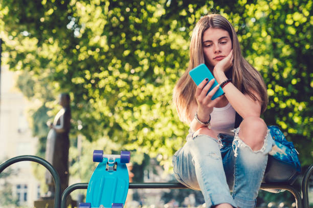 girl with skateboard in the city park text messaging - hipster people surfing the net internet imagens e fotografias de stock