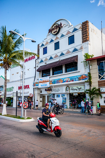 Cozumel, Mexico - December 29, 2016: Man on motorcycle on Cozumel street with shops and tourists on background