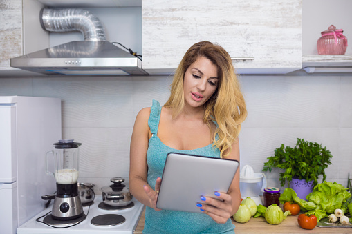 Attractive young woman use digital tablet in her kitchen