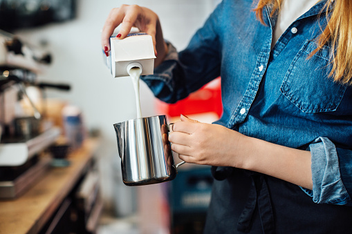 Female barista pouring milk into jug at cafe