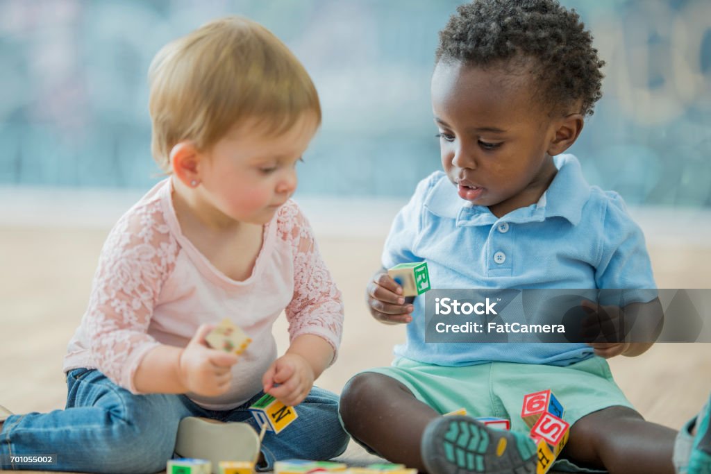 Having a Good Time African-American baby boy playing with Caucasian infant girl on the carpet in the daycare. Baby - Human Age Stock Photo