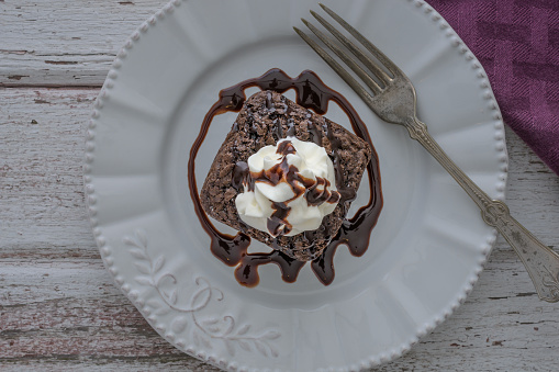 Overhead view of a Single Chocoate Brownie on Plate topped with whip cream and chocolate Syrup