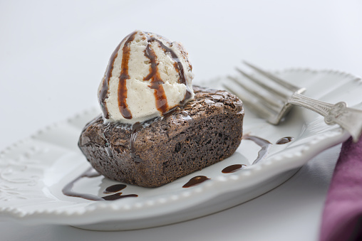 Single Chocoate Brownie on Plate topped with Ice Cream and Chocolate Syrup.