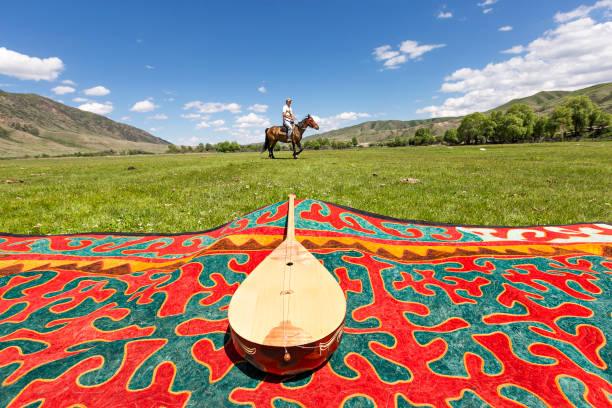Dombra, local musical instrument, Saty Village, Kazakhstan. Saty Village, Kazakhstan - June 3, 2017: Kazakh musical instrument of Dombra on a carpet with a man on horse in the background, in Saty Village, Kazakhstan. almaty photos stock pictures, royalty-free photos & images