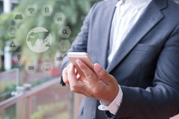 istock businessman in suit holding smart phone while standing outside building. young asian male using cellphone for work at modern office corridor with communication and internet icon 701152364