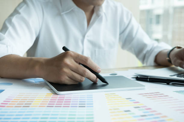 istock young graphic designer working with computer and color swatch. creative man using stylus pen and digital tablet at modern office. Architect using work tools and sample colour catalog. business, technology, design and people concept 701152368