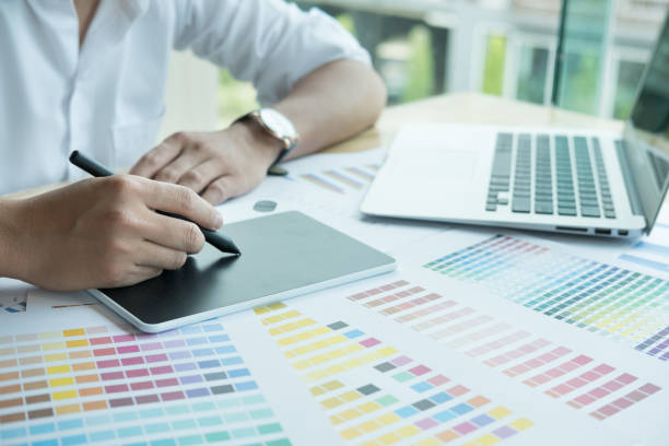istock young graphic designer working with computer and color swatch. creative man using stylus pen and digital tablet at modern office. Architect using work tools and sample colour catalog. business, technology, design and people concept 701152376