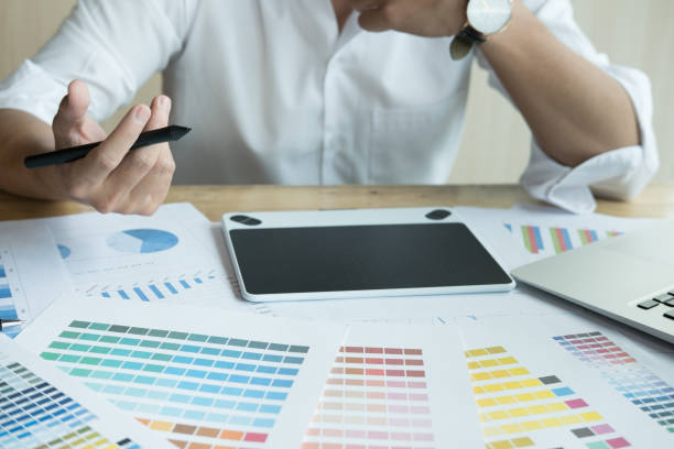 istock young graphic designer working with computer and color swatch. creative man using stylus pen and digital tablet at modern office. Architect using work tools and sample colour catalog. business, technology, design and people concept 701152398