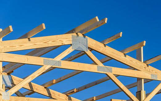 Roof with a wooden truss framework with a blue sky background.
