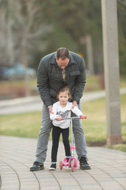 istock Dad helping young daughter learn to ride scooter 701193244
